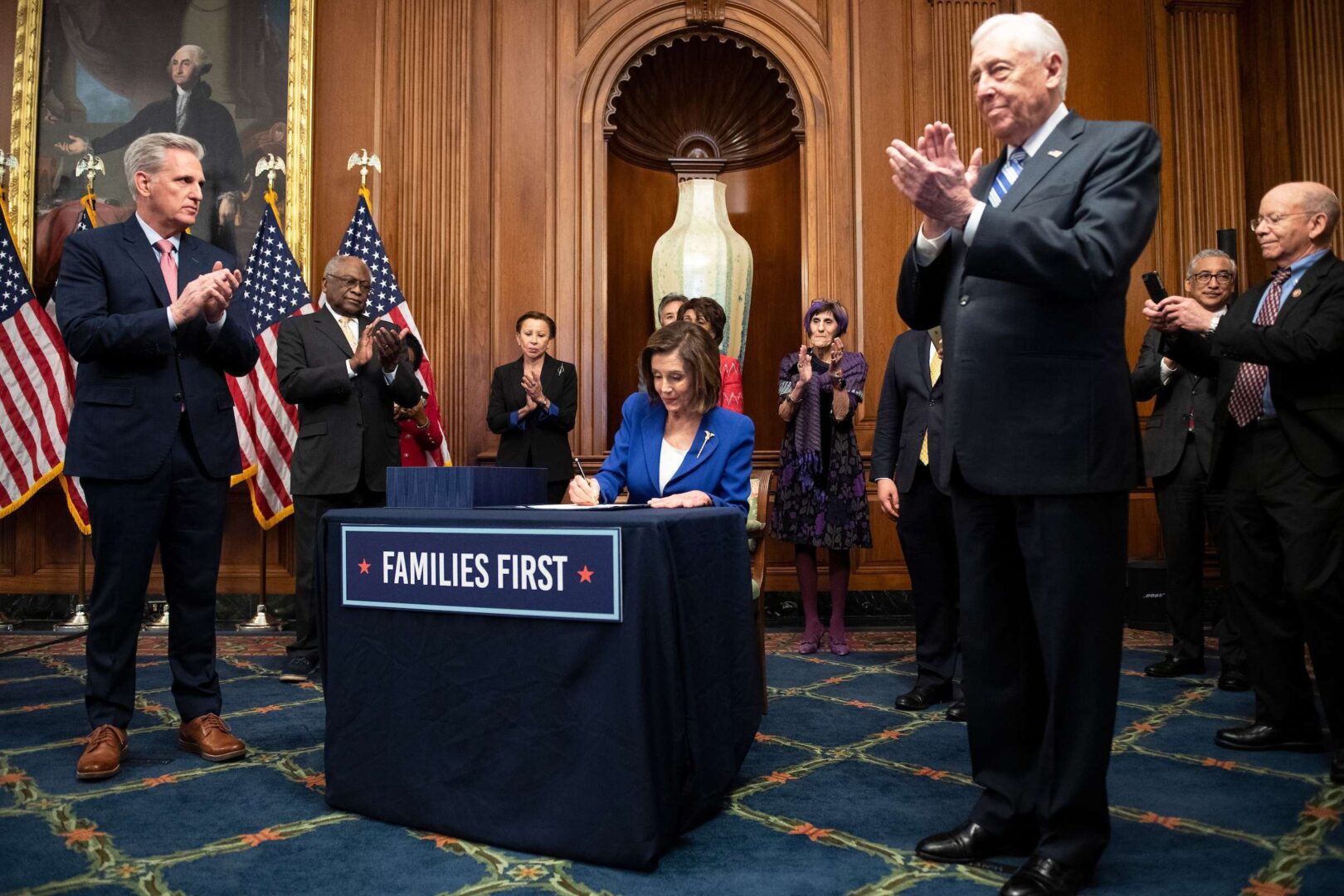 Speaker Nancy Pelosi signs the coronavirus stimulus bill Friday after it passed the House. Also pictured around her, from left, are Minority Leader Kevin McCarthy, Majority Whip James E. Clyburn, Rep. Nydia M. Velázquez, Rep. Rosa DeLauro, Majority Leader Steny H. Hoyer, Rep. Bobby Scott and Rep. Peter DeFazio. 
