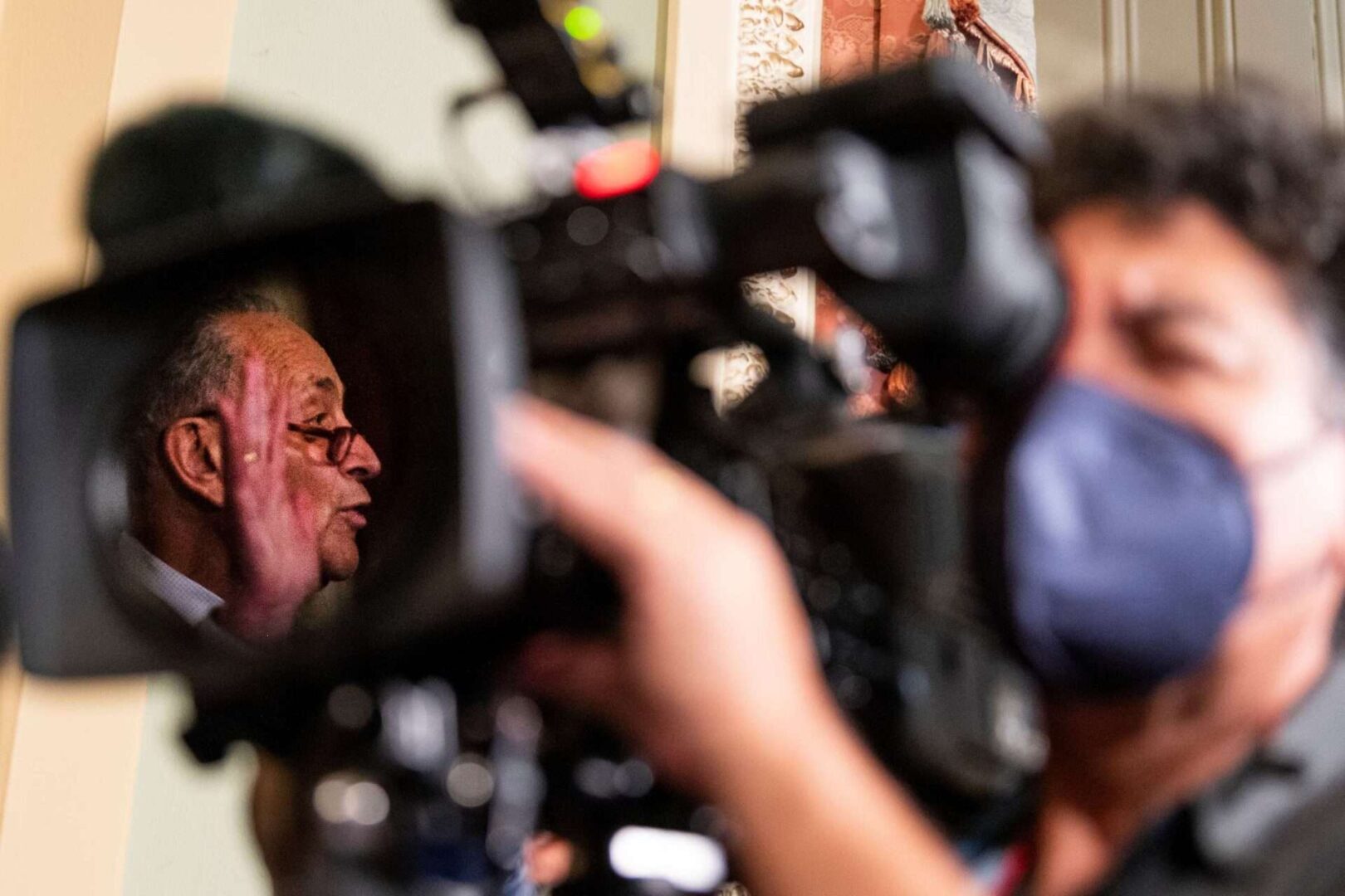 UNITED STATES - OCTOBER 5: Senate Majority Leader Chuck Schumer, D-N.Y., is reflected in a TV camera lens as he holds his weekly press conference in the Ohio Clock Corridor in the Capitol on Tuesday, Oct. 5, 2021. (Photo by Bill Clark/CQ Roll Call)