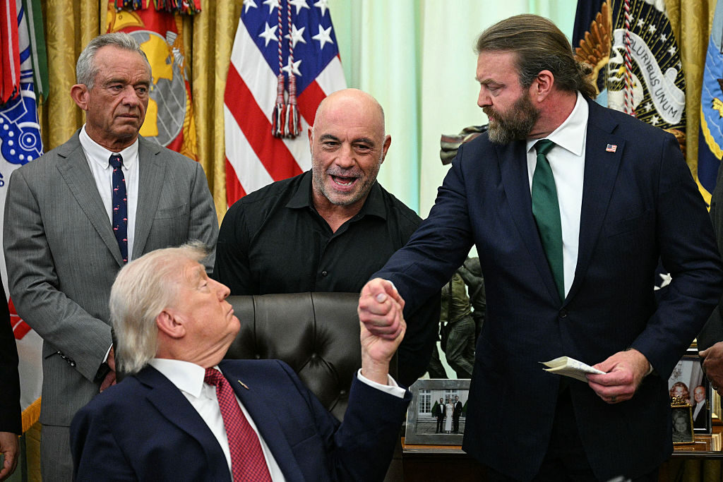 HHS Secretary Robert F. Kennedy Jr. and podcaster Joe Rogan look on as President Donald Trump shakes hands with W. Bryan Hubbard, CEO of Americans for Ibogaine, during an executive order signing ceremony at the White House on April 18. The executive order aims to further medical research and clinical trials for certain psychedelic drugs. The use of psychedelics is a theme in the Thomas Pynchon novel “The Crying of Lot 49,” one of many parallels in the book to our current time, Political Theater discusses. 